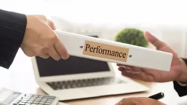 Two hands exchanging a binder labeled 'Performance' in an office setting.