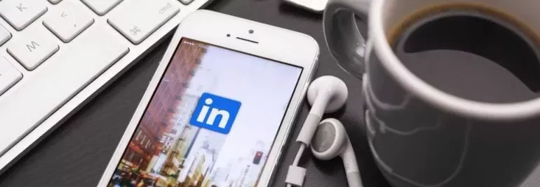 Smartphone displaying LinkedIn app next to a keyboard and coffee.