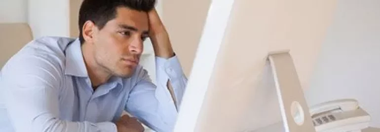 Homme assis à un bureau, regardant stressé un écran d'ordinateur.